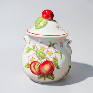 Her Good Eye decorative ceramic jar with hand-painted apple and blossom design, red apple finial on lid.