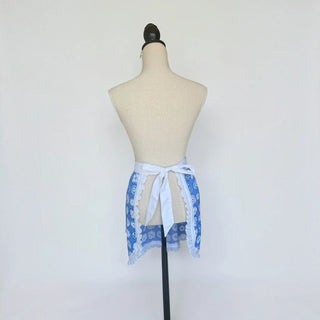 Her Good Eye blue floral half apron with white waistband and lace trim, shown from the back on a mannequin.