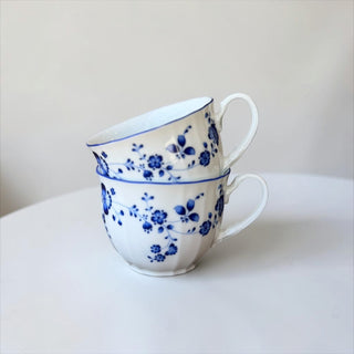 Her Good Eye white porcelain teacup and saucer set with blue floral pattern and scalloped edges.