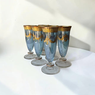 Set of six Her Good Eye blue glass goblets with ornate gold trim and garland detailing. Vintage-inspired stemmed glasses.