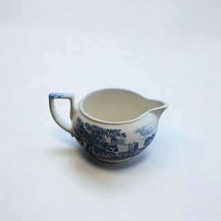 Her Good Eye blue and white ceramic creamer pitcher with landscape pattern and blue handle detail.