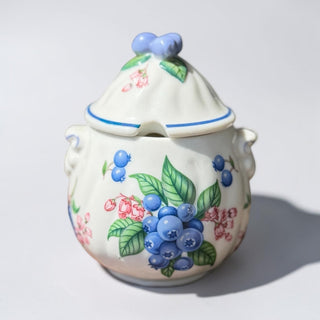 Her Good Eye white ceramic sugar bowl with blueberry pattern, lid, and blue bow detail. Features spoon notch.