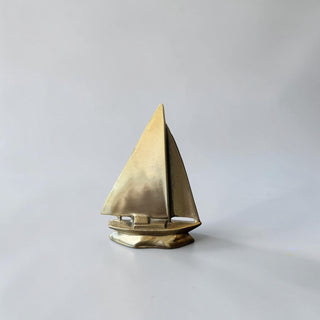 Her Good Eye polished brass sailboat figurine with a triangular sail and detailed hull, a nautical decorative object.