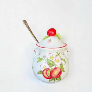Her Good Eye ceramic sugar bowl with apple motif, white glaze, red trim, and a cherry lid finial with serving spoon.