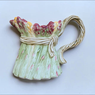 Her Good Eye ceramic asparagus pitcher featuring textured green stalks, burgundy tips, and a decorative tied band.