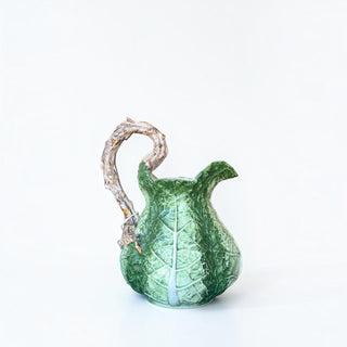 Her Good Eye ceramic cabbage leaf pitcher with a textured green body and a sculpted gnarled branch handle.