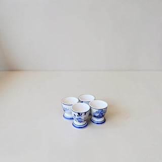 Her Good Eye set of four white ceramic egg cups with hand-painted blue floral and windmill Dutch pottery motifs.