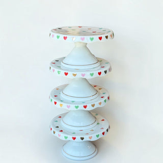 Her Good Eye ceramic cake stand stack featuring a glossy white finish with colorful heart patterns on the scalloped rim.