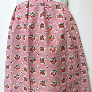 Her Good Eye pink cotton half apron with cherry and strawberry print and white eyelet lace trim.