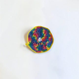 Her Good Eye handmade circular crochet coaster in vibrant multi-colored yarn with a bright yellow border.