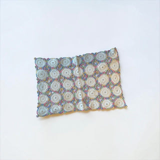 Her Good Eye handmade crochet table runner with white floral motifs and variegated pastel blue, pink, and yellow borders.