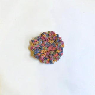 Her Good Eye handmade crochet flower coaster in vibrant multi-colored variegated cotton yarn with textured design.