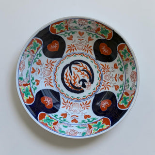 Her Good Eye decorative ceramic plate with intricate blue, orange, green, and white floral and heart motifs.