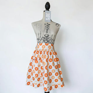 Her Good Eye donut print cotton kitchen apron with pockets and lace trim, white with orange and peach donuts.