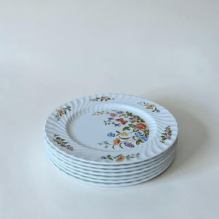 Her Good Eye white ceramic dinner plate with a hand-painted floral and butterfly design and swirled rim.