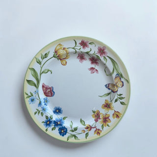 Her Good Eye ceramic dinner plate with hand-painted yellow, pink, and blue flowers and butterflies. Features a yellow rim and green border.