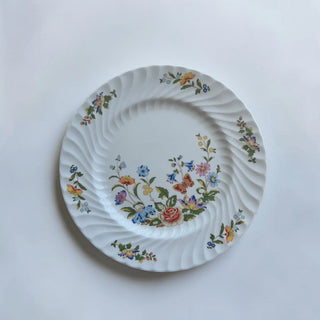 Her Good Eye white ceramic dinner plate with hand-painted floral and butterfly motif and swirled rim.