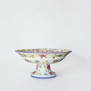 Her Good Eye hand-painted ceramic pedestal bowl with vibrant pink, yellow, and violet floral motifs and purple rim.
