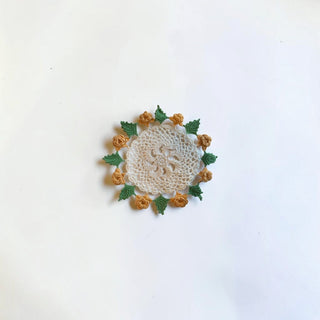 Her Good Eye handmade crochet doily with a white lace center and a border of yellow roses and green leaves.