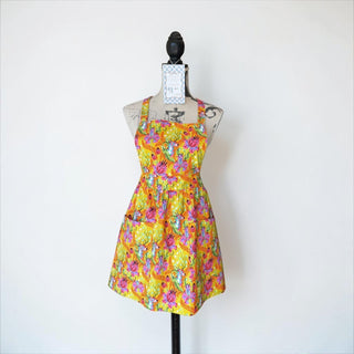 Her Good Eye floral deer print kitchen apron in yellow with pink and purple flowers. Features two front pockets and adjustable straps.