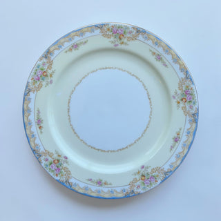 Her Good Eye floral pattern dinner plate with blue rim, pink and blue blossoms, gold scrollwork on creamy yellow porcelain.