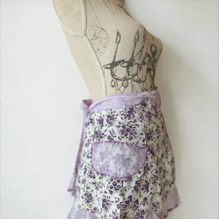Her Good Eye floral print ruffled half apron with purple wildflowers on white cotton blend, lavender trim and pocket.