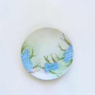 Her Good Eye porcelain plate featuring hand-painted blue forget-me-not flowers on a sage green and cream background.
