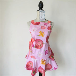 Her Good Eye light pink cotton blend apron with floral print, ruffles, and coral bow accent. Features daisies and abstract circular motifs.