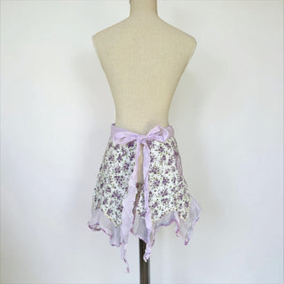 Her Good Eye floral print ruffled half apron with purple wildflowers on white and lavender trim. Cotton blend.