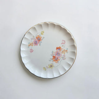 Her Good Eye floral dessert plate with scalloped edge and gold trim, featuring pink, orange, yellow, and lavender flowers.