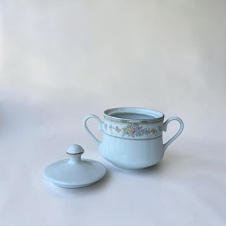 Her Good Eye light blue porcelain sugar bowl with lid, featuring a delicate floral band with pastel flowers and gold trim.