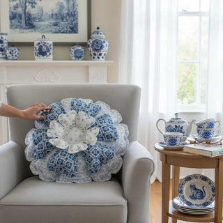 Her Good Eye blue and white floral-shaped throw pillow with layered petal design on a grey armchair.