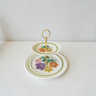 Her Good Eye two-tiered ceramic serving tray with vintage floral print, gold handle, and green banding.