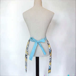 Her Good Eye yellow half apron with garden scene print and sky-blue ties. Cotton blend.