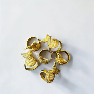 Her Good Eye set of six gold metal pineapple napkin rings with textured detail and leafy crown.