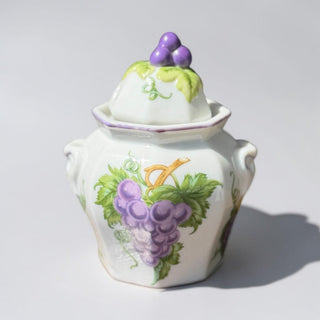 Her Good Eye white ceramic jar with purple grapes and green leaves motif, grape finial, and purple trim.