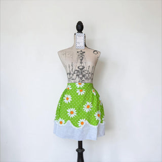 Her Good Eye green cotton half apron with white daisies, orange centers, white polka dots, and lace trim.