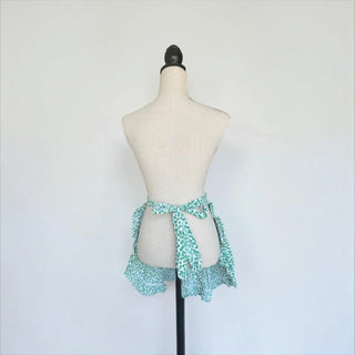 Her Good Eye green and white floral half apron with a ruffled hem and adjustable waist tie on a mannequin