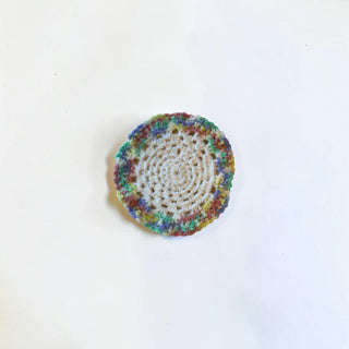 Her Good Eye handmade round crochet coaster with a cream center and vibrant variegated multi-colored yarn border.