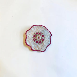 Her Good Eye handmade white cotton crochet doily with vibrant magenta floral motifs and a scalloped border.
