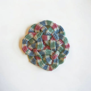 Her Good Eye handmade crochet coaster in variegated sage green, dusty rose, and slate blue with an intricate knot design