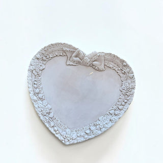 Her Good Eye heart-shaped ceramic tray with embossed floral border and ribbon bow detail in a soft neutral finish.