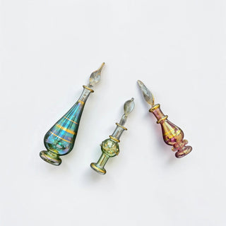 Her Good Eye iridescent glass perfume bottles with gold-tone accents and tapered stoppers on a white background
