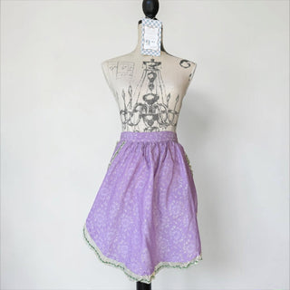 Her Good Eye lavender cotton blend half apron with floral print, silver threads, lace, and green ribbon trim.