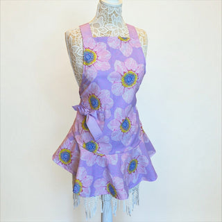 Her Good Eye lavender kitchen apron with pink and yellow floral print, ruffled hem, and side bow on a dress form.