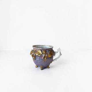 Her Good Eye lavender porcelain footed cup with ornate hand-painted gold leaf floral relief and curved handle.
