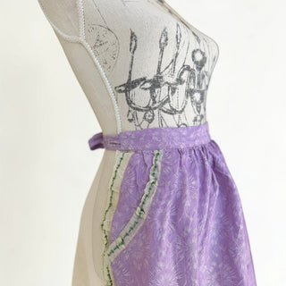 Her Good Eye lavender cotton blend half apron with floral print, silver threads, lace trim, green ribbon, and two pockets.