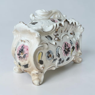 Her Good Eye ornate ceramic trinket box with pink and blue floral motifs and gold trim. Features scrollwork and raised designs.