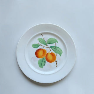 Her Good Eye ceramic dinner plate featuring a hand-painted peach motif with green leaves on a white background.