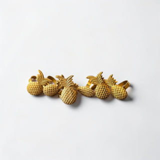 Her Good Eye set of six gold metal pineapple napkin rings with textured detail and leafy crowns.